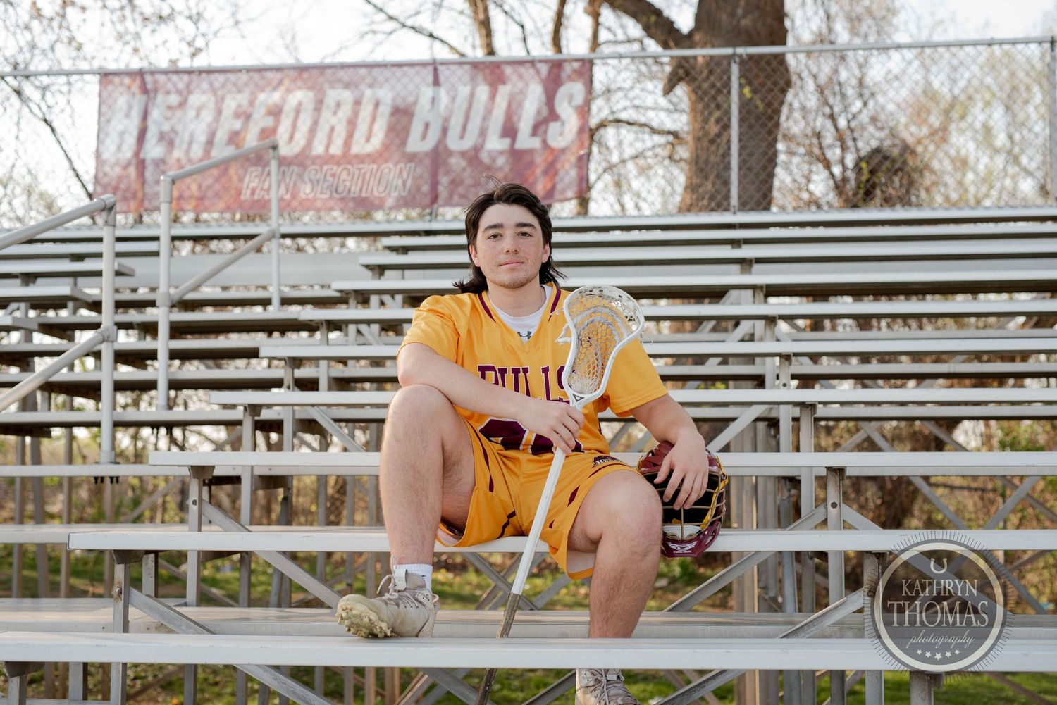 Baseball player in yellow uniform sits on metal bleachers at baseball field.