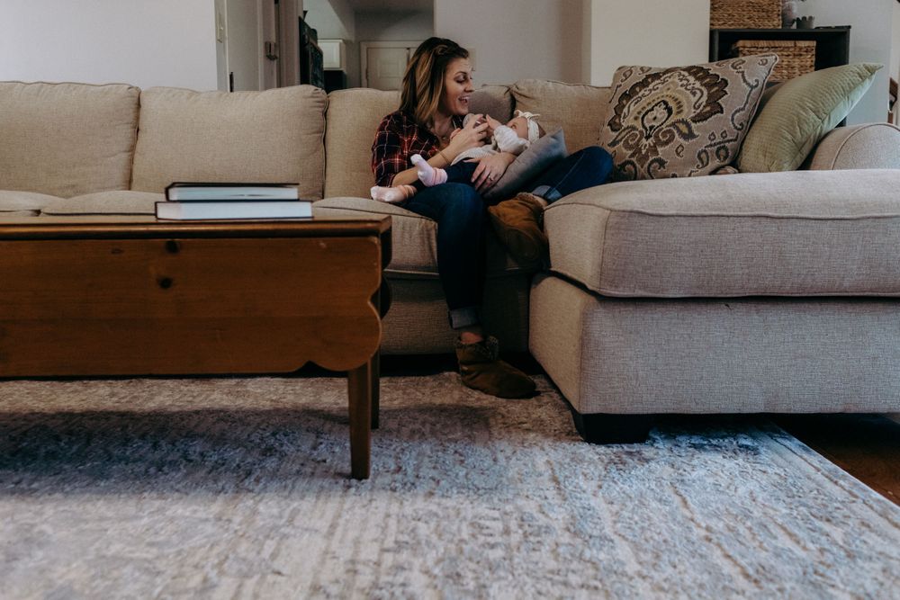 A mother and baby relaxing together on a gray sectional sofa with a decorative area rug.