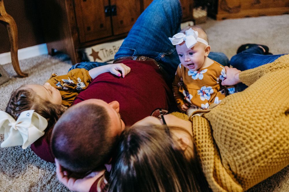 Family lounging together on floor with yellow blanket and casual attire.