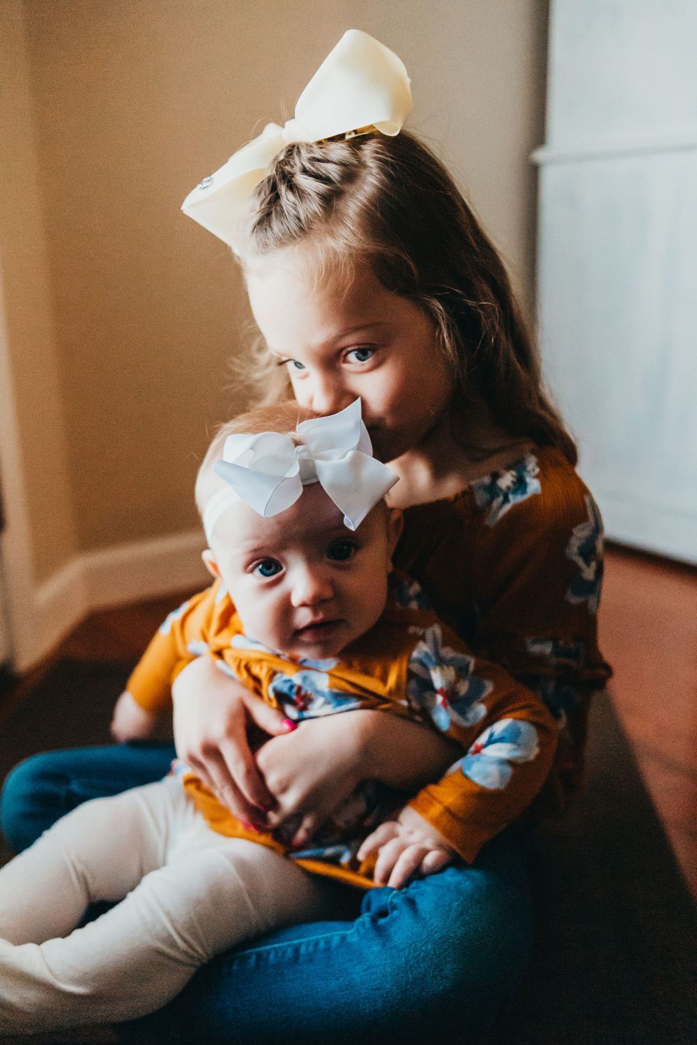 Sweet sisterly moment with matching white bows and floral outfits.