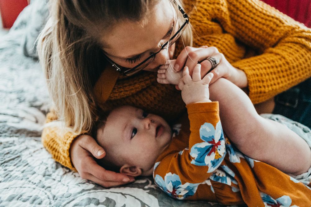 Intimate family moment captured on gray bedding with yellow sweater details.