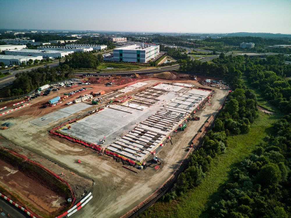 Drone shot of a large-scale construction site with white foundation work surrounded by green landscape.