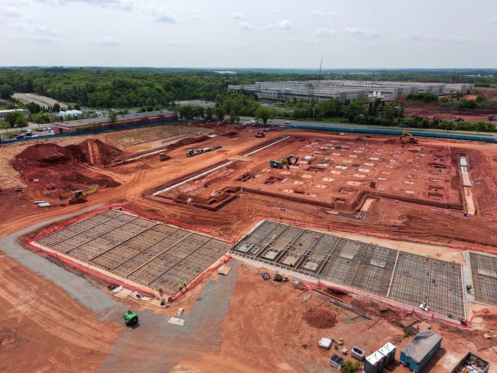 Drone photograph of a large construction site with red clay soil and concrete foundation sections.