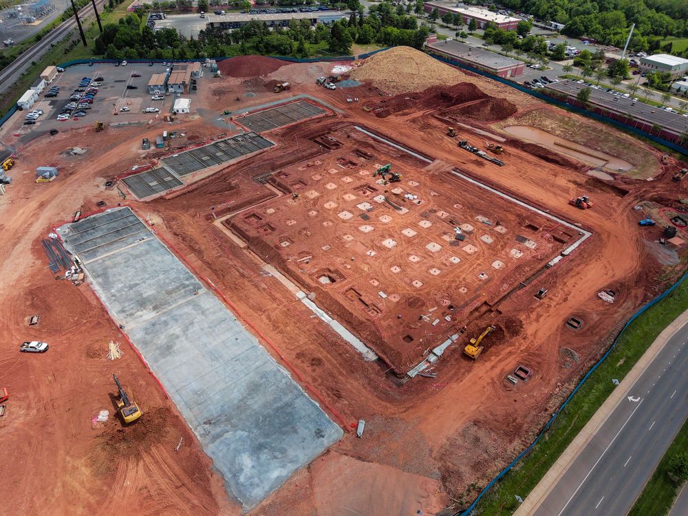 Aerial view of a construction site with red soil and concrete foundation work.