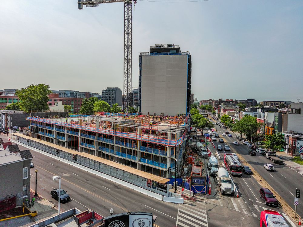 Construction progress of a multi-story building with exposed floors and a tower crane overhead.