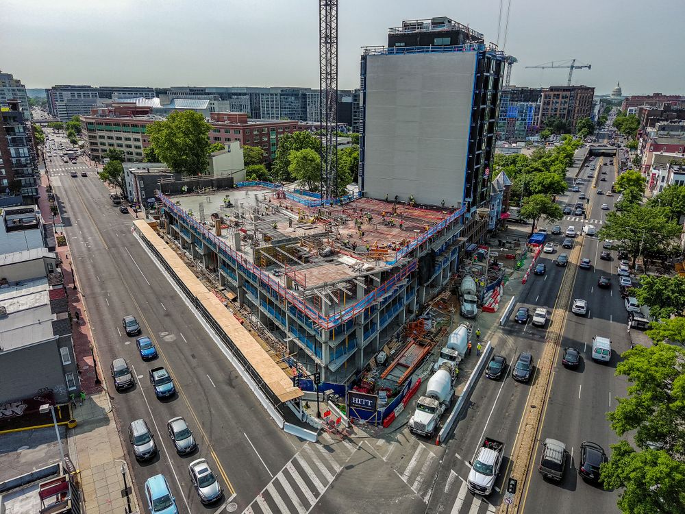 Bird's eye view of a corner construction site in a busy urban intersection with traffic.