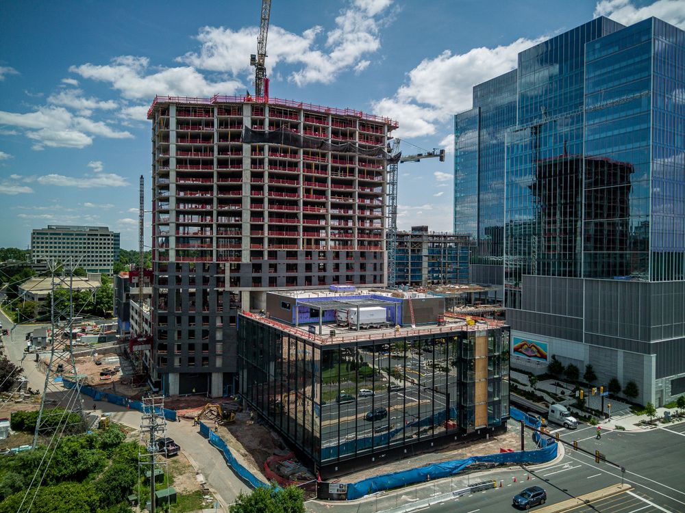 High-rise construction project with tower crane against blue sky and glass office buildings.