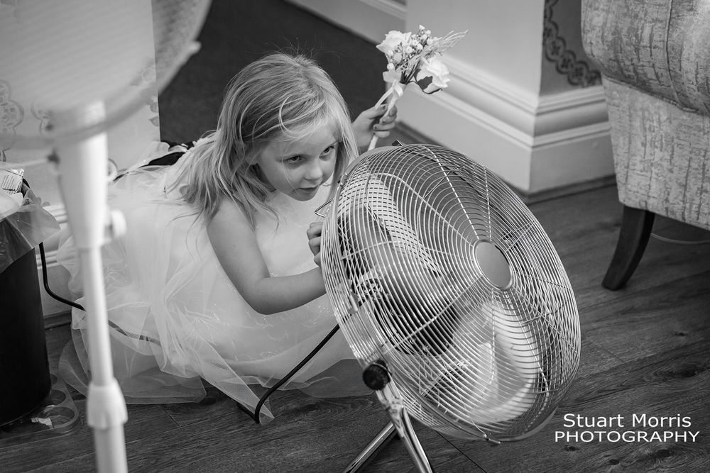 Young flower girl cools down with a large floor fan. Country house hotel wedding photographer. Lancashire wedding venue.