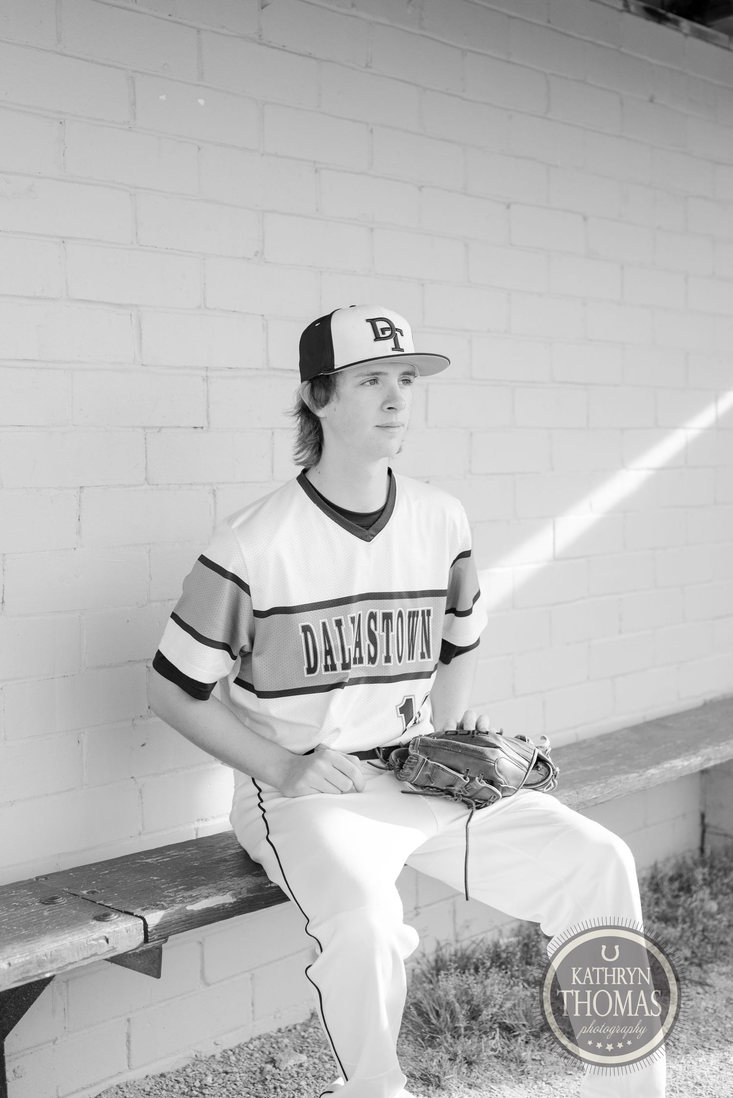 Baseball player in white uniform sits in dugout for black and white portrait.