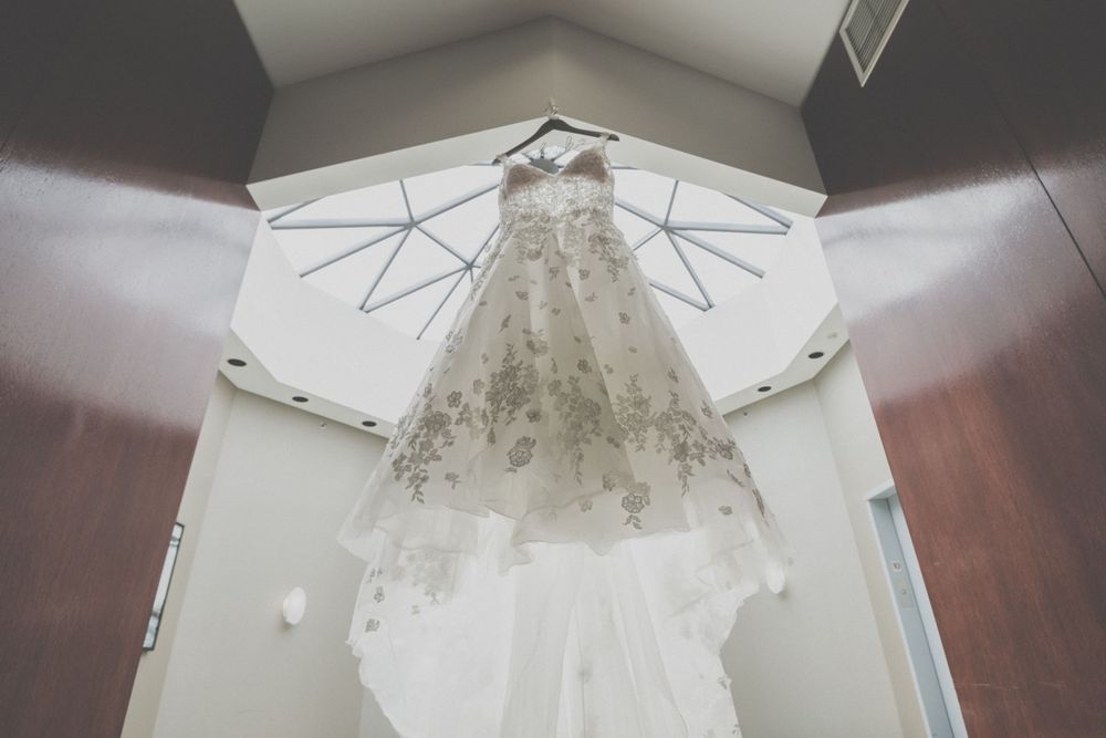 White wedding dress hanging against a light background showing intricate lace patterns.