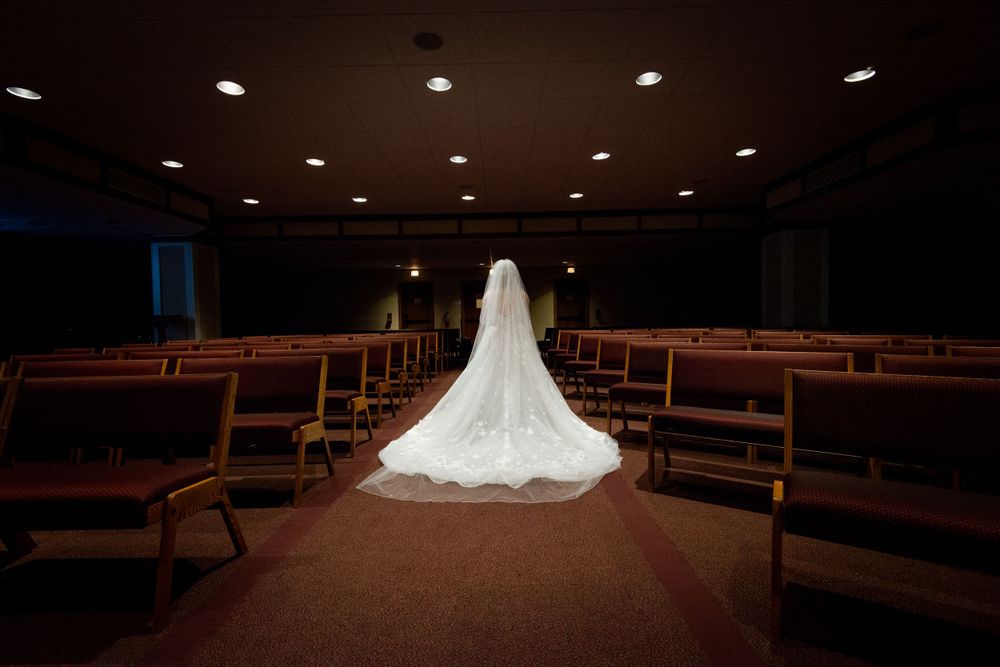 Wide angle view of empty church pews with dramatic lighting and a wedding dress in focus.