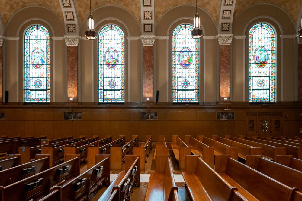 Ornate church interior with stained glass windows and wooden pews in warm lighting.