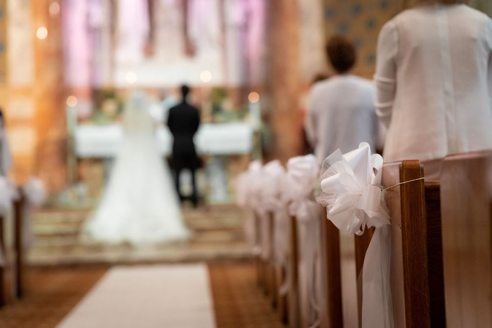 Church aisle decorated with white bows and natural light streaming through stained glass windows.
