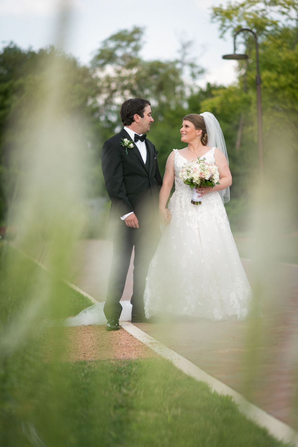 Wedding couple photographed through foliage in an outdoor garden setting.