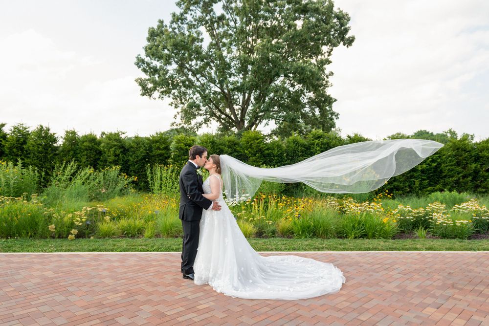 Wedding couple walking along brick pathway surrounded by lush summer greenery.
