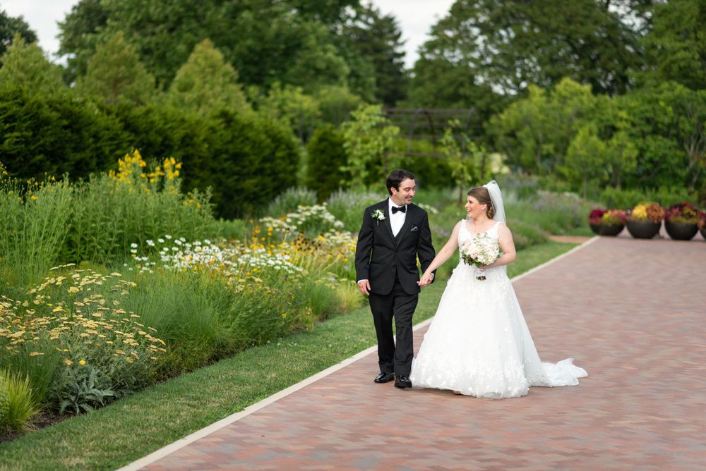 Bride and groom pose in garden setting with yellow wildflowers and brick pathway.