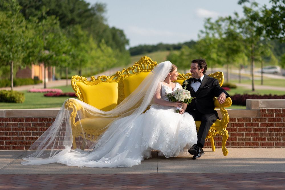 Wedding couple photographed against yellow flowers and brick wall with flowing veil.