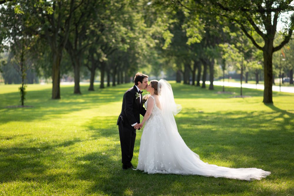 Wedding couple walking through sunlit park with trees creating natural backdrop.