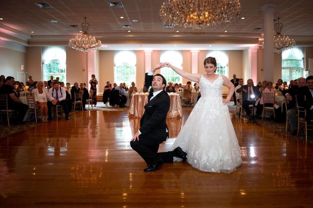 Wedding reception dance floor in an elegant ballroom with pink accent lighting and large windows.