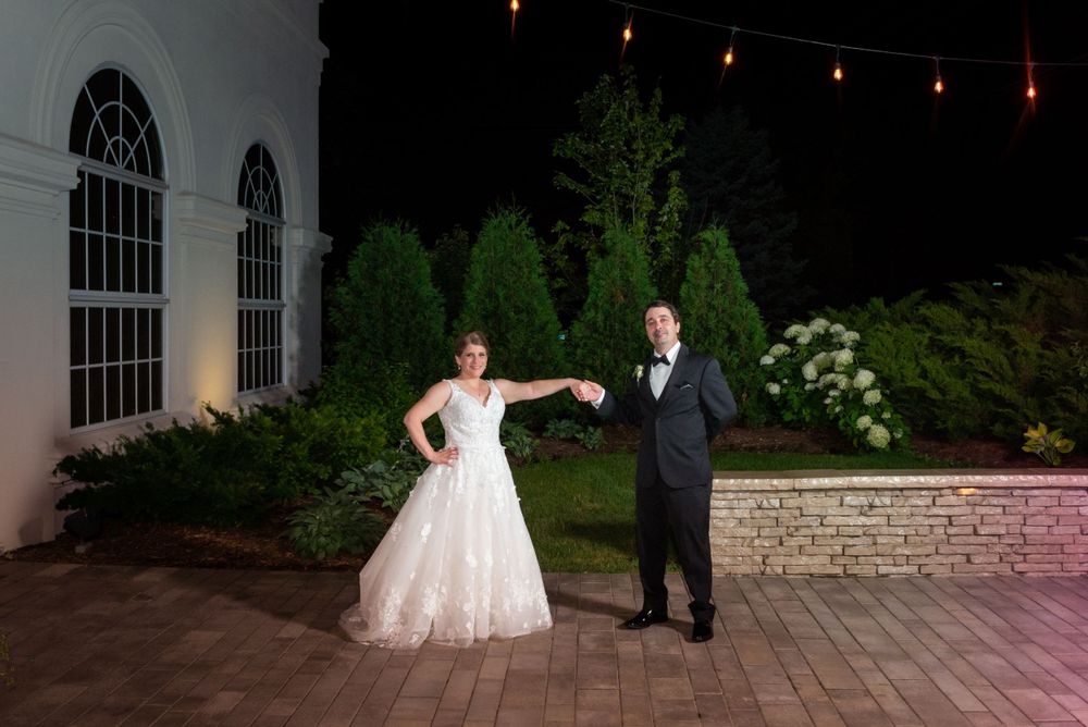 Romantic nighttime wedding photos with string lights illuminating a stone patio and building exterior.