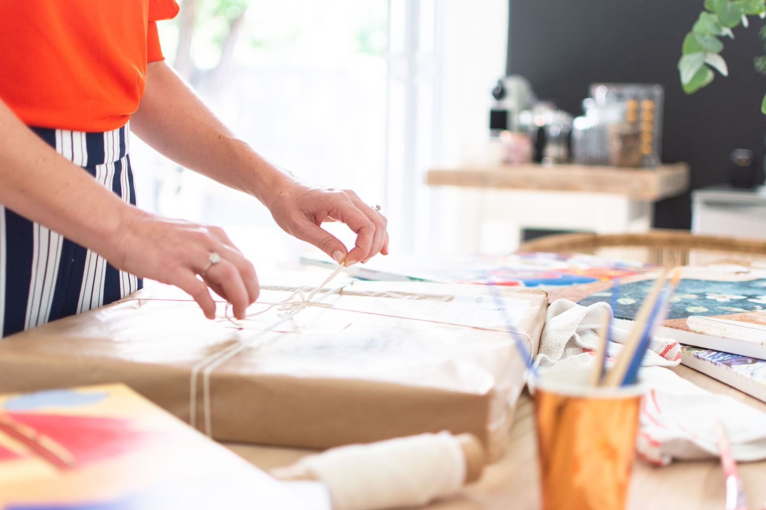 Hands packaging items on wooden table with shipping materials and supplies.