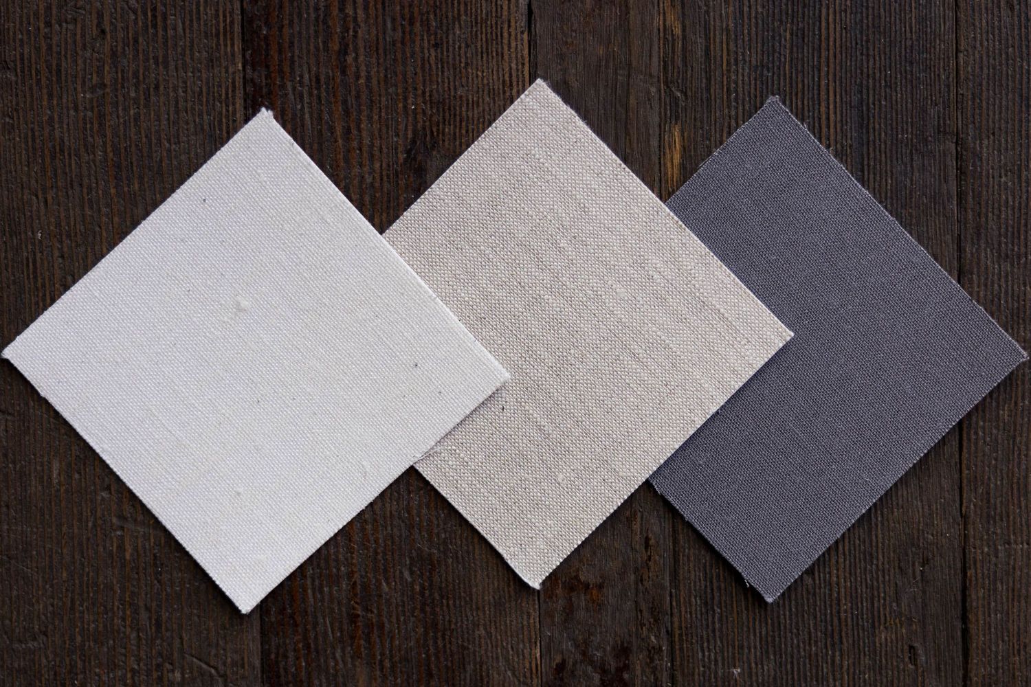 Three linen fabric samples in white, beige, and gray arranged on dark wood.