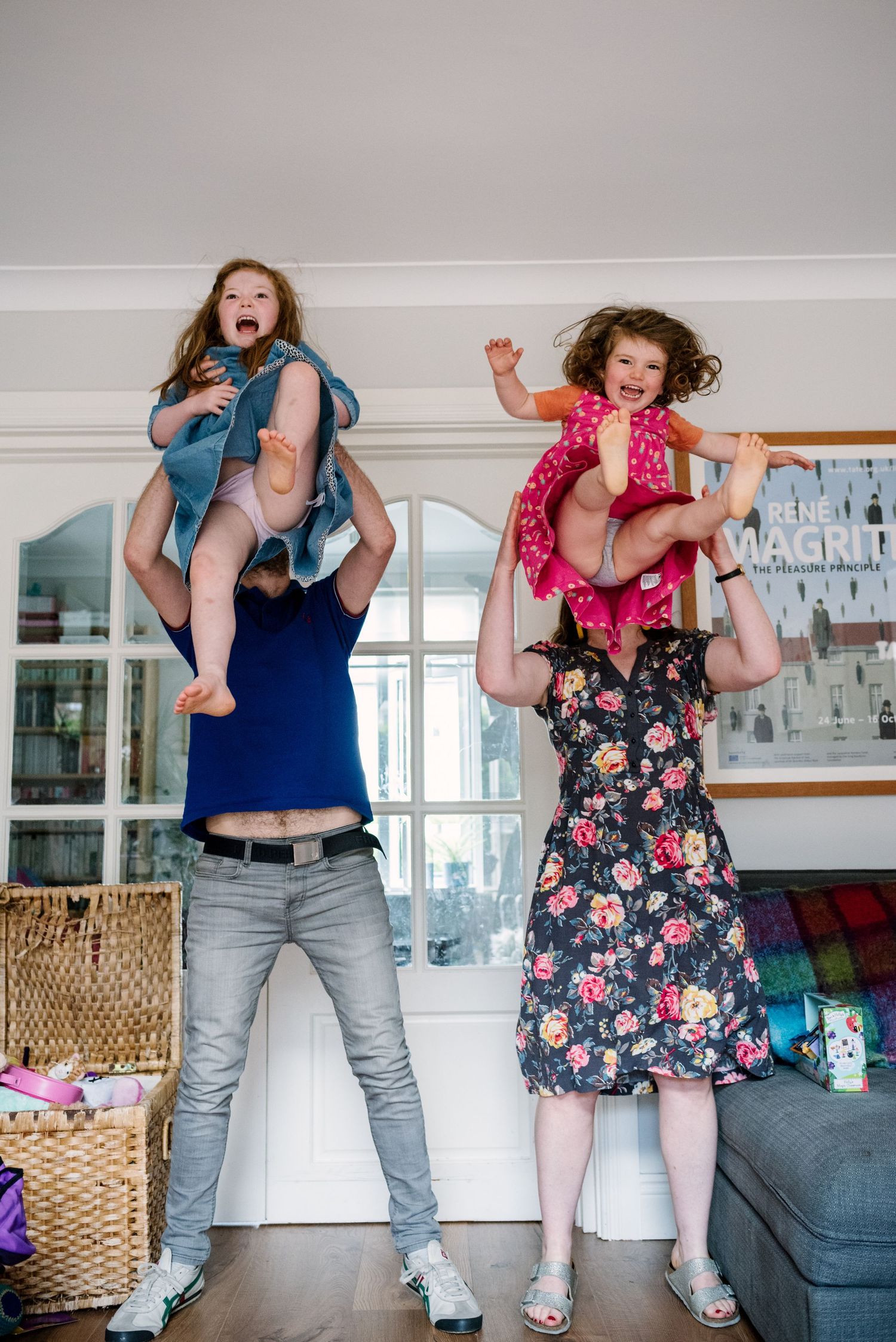 Playful indoor scene of adults lifting children overhead in a living room.