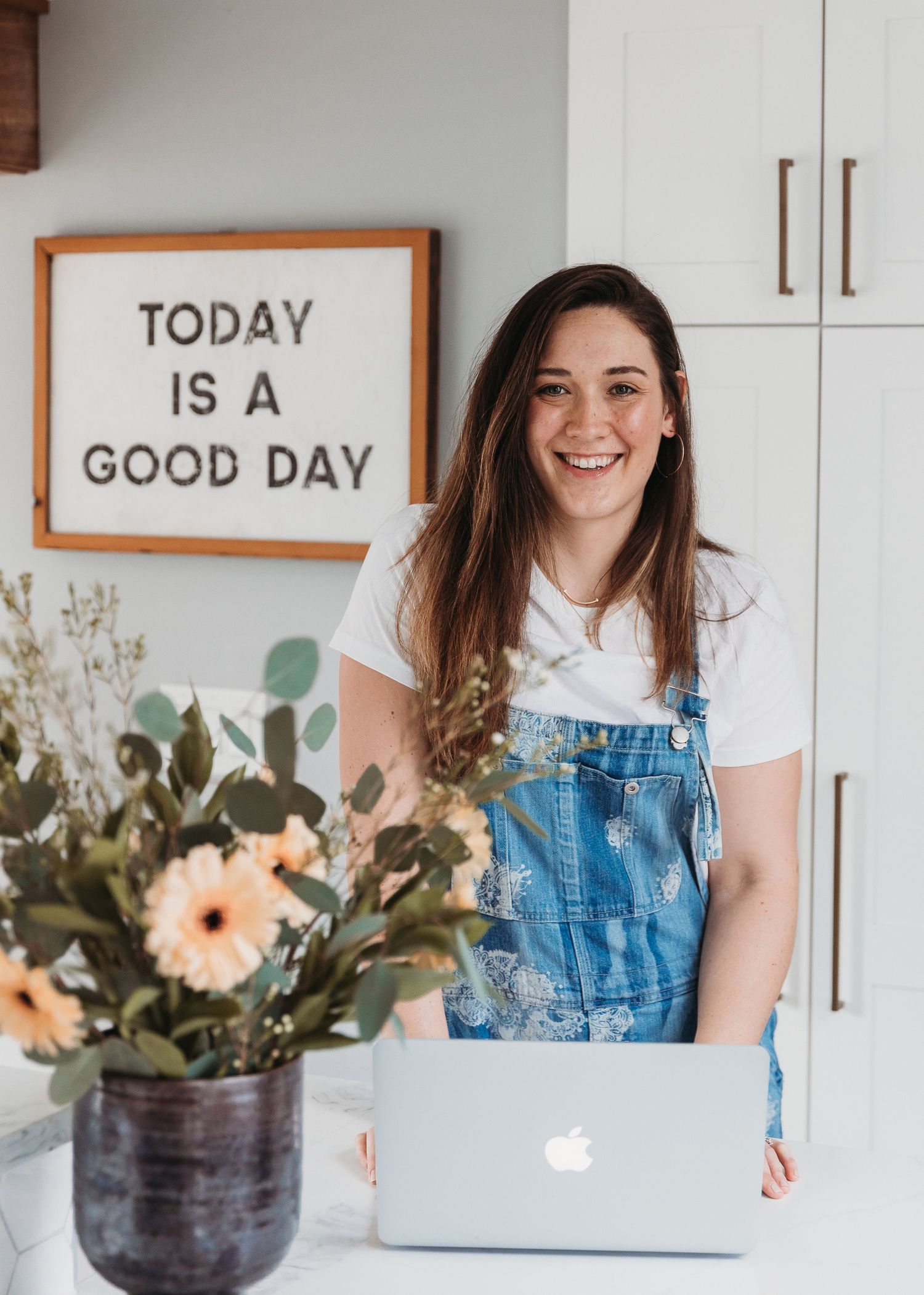 Bright kitchen workspace with laptop, flowers and motivational sign.