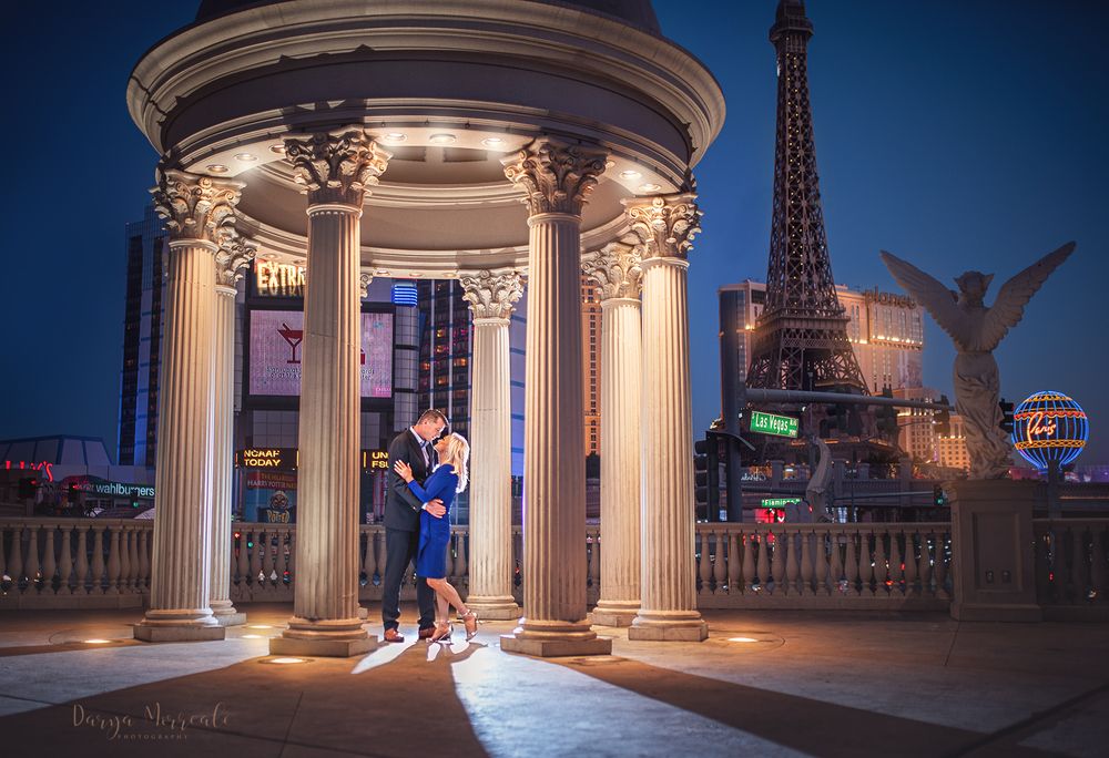 A couple embraces in a column-lined gazebo with the Las Vegas strip visible in background.