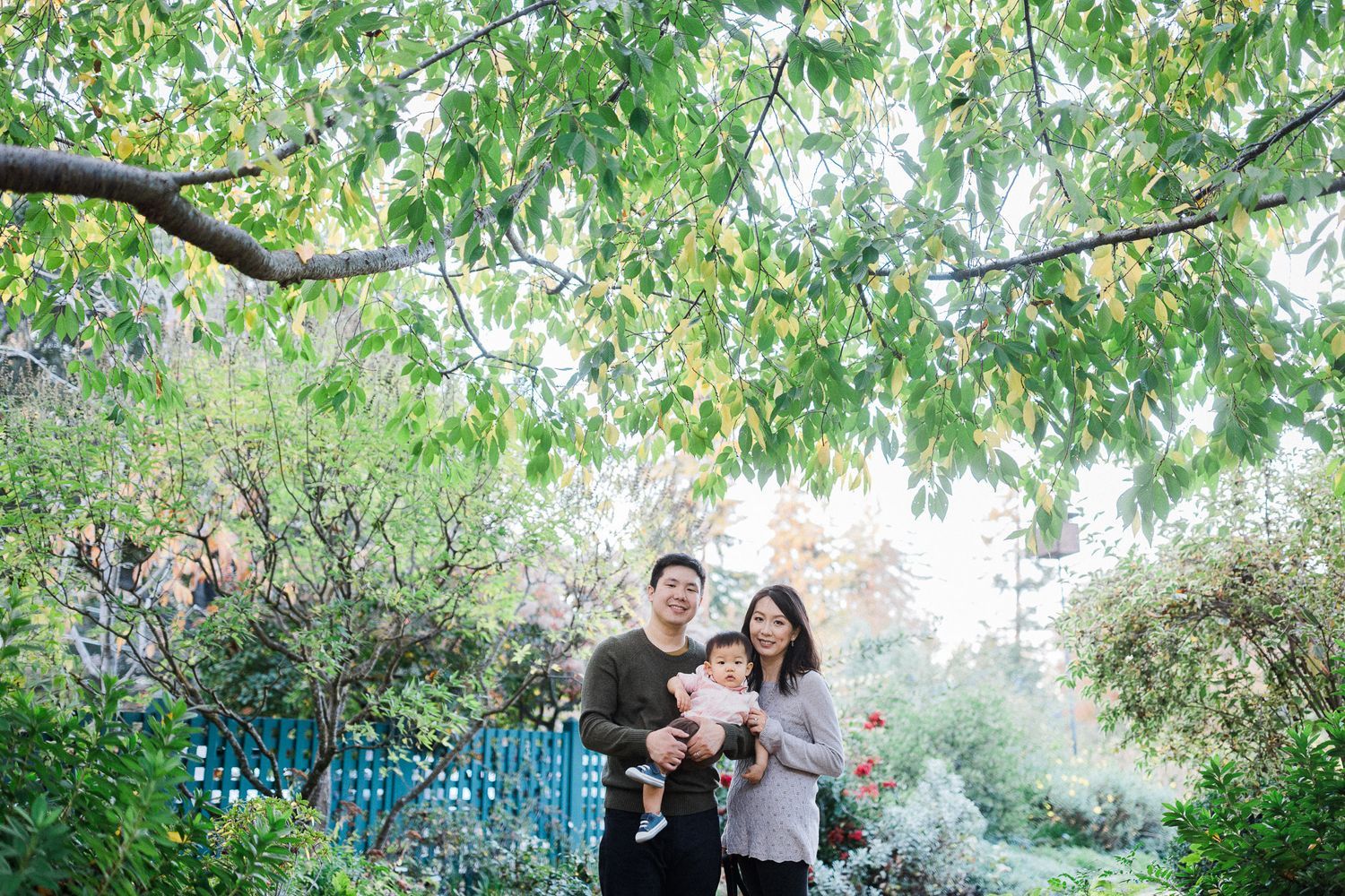 A family portrait captured in a lush garden setting with green foliage and blue decorative elements.