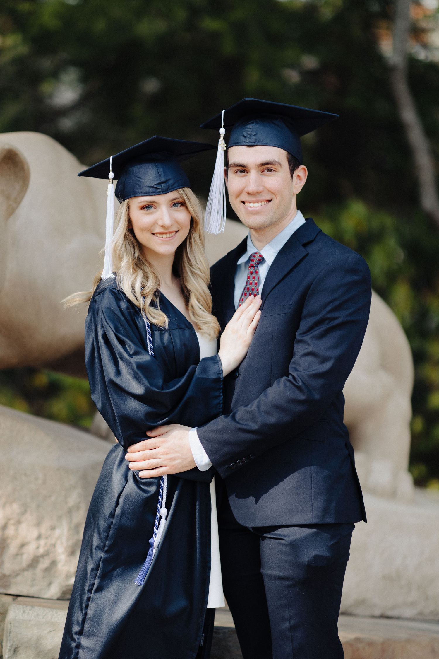 Graduation couple poses together in front of campus lion statue.