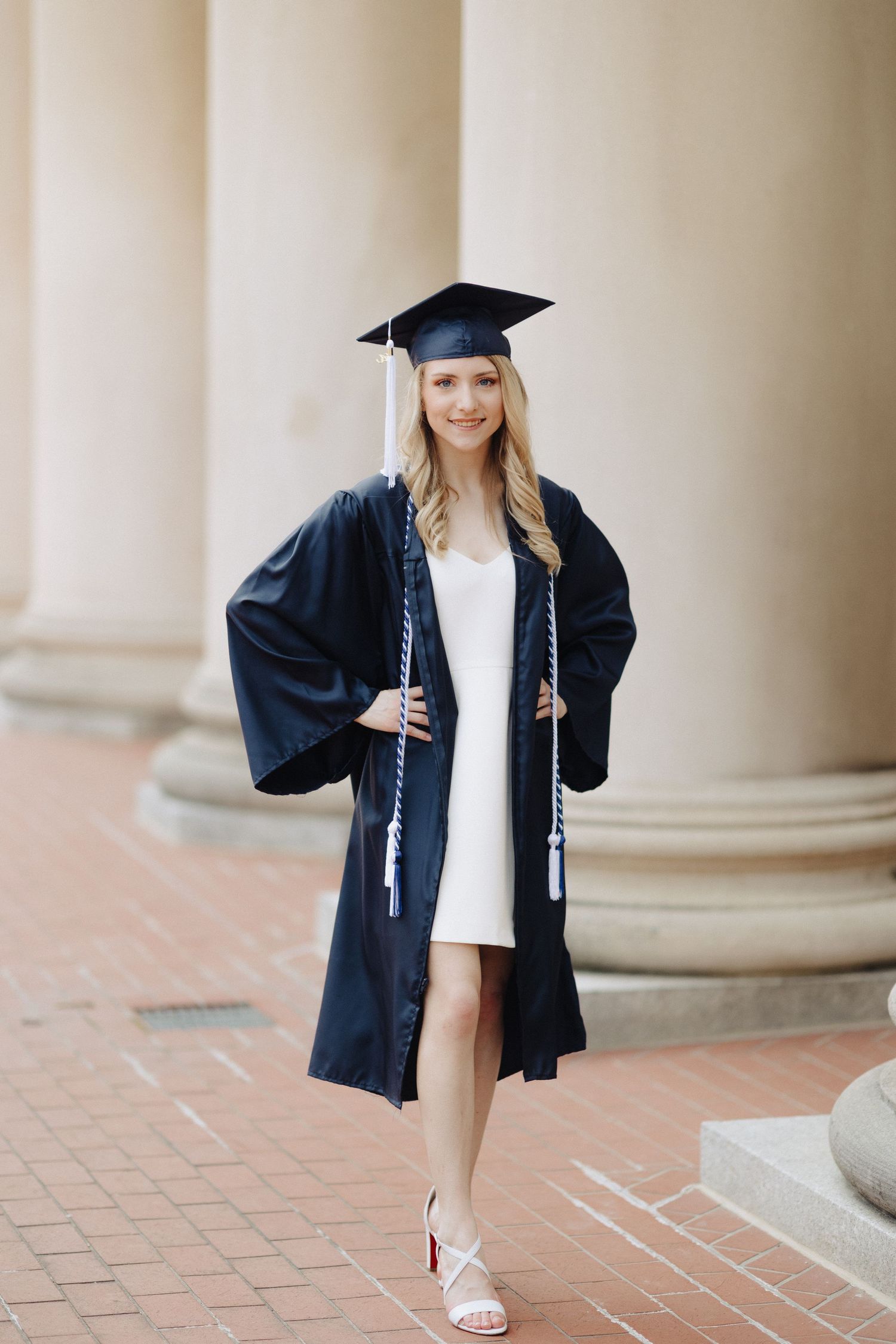 Graduate in navy graduation attire poses elegantly by classic architecture.