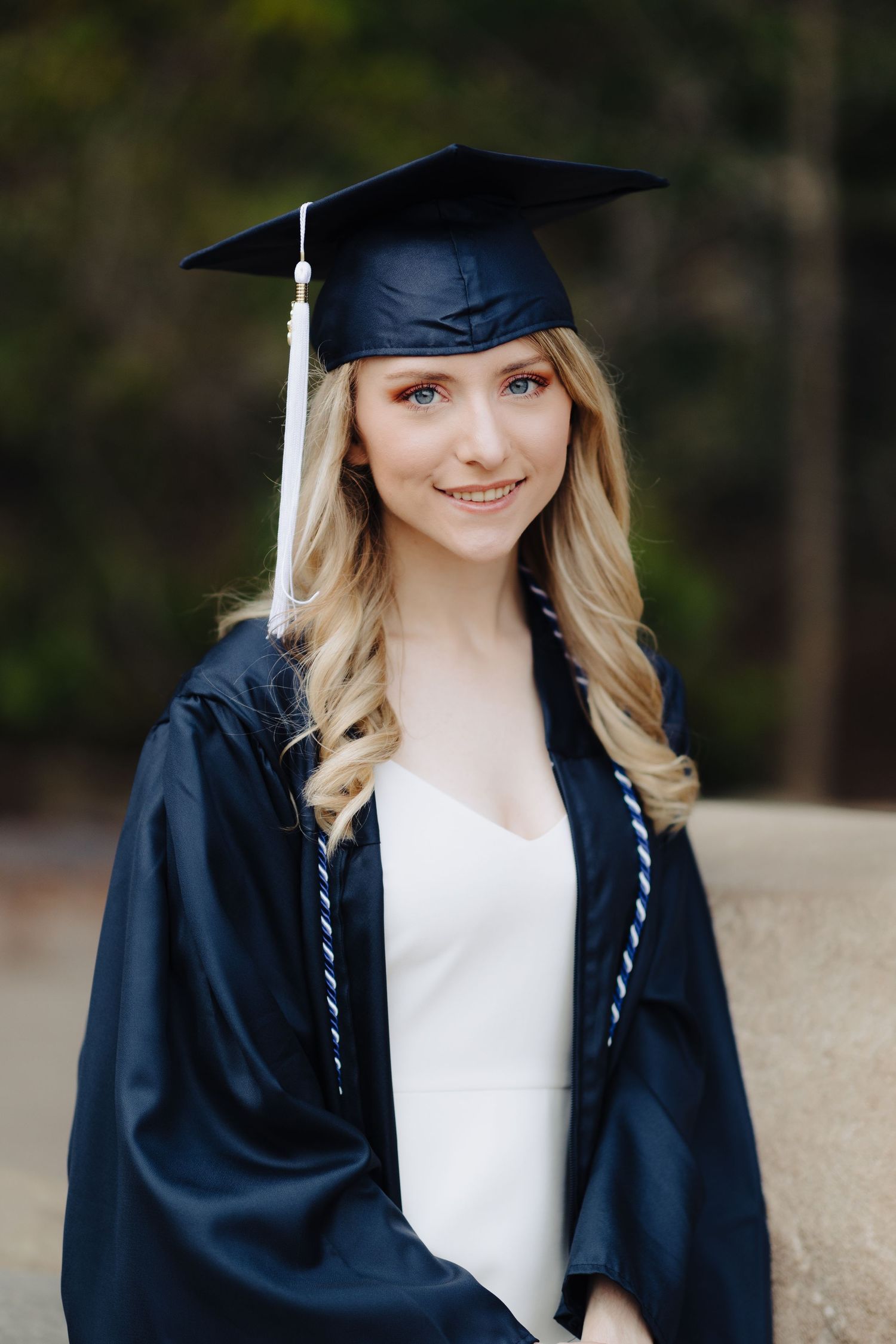 Academic portrait of graduate in traditional cap and gown against natural background.