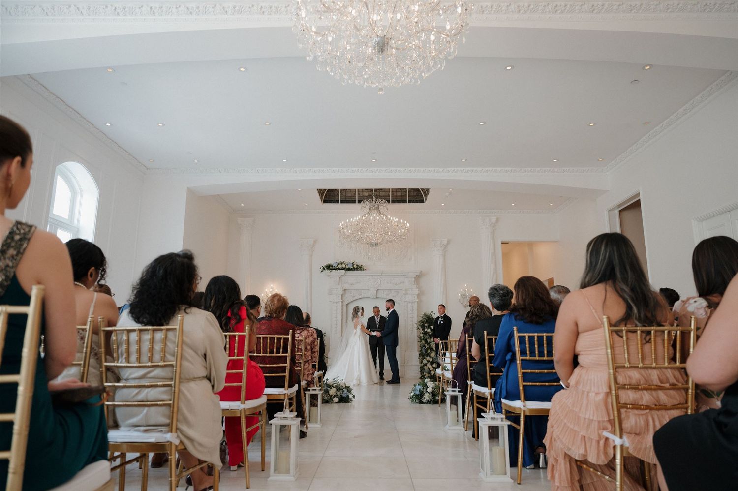 Wedding guests seated in rows watching a ceremony under a crystal chandelier.