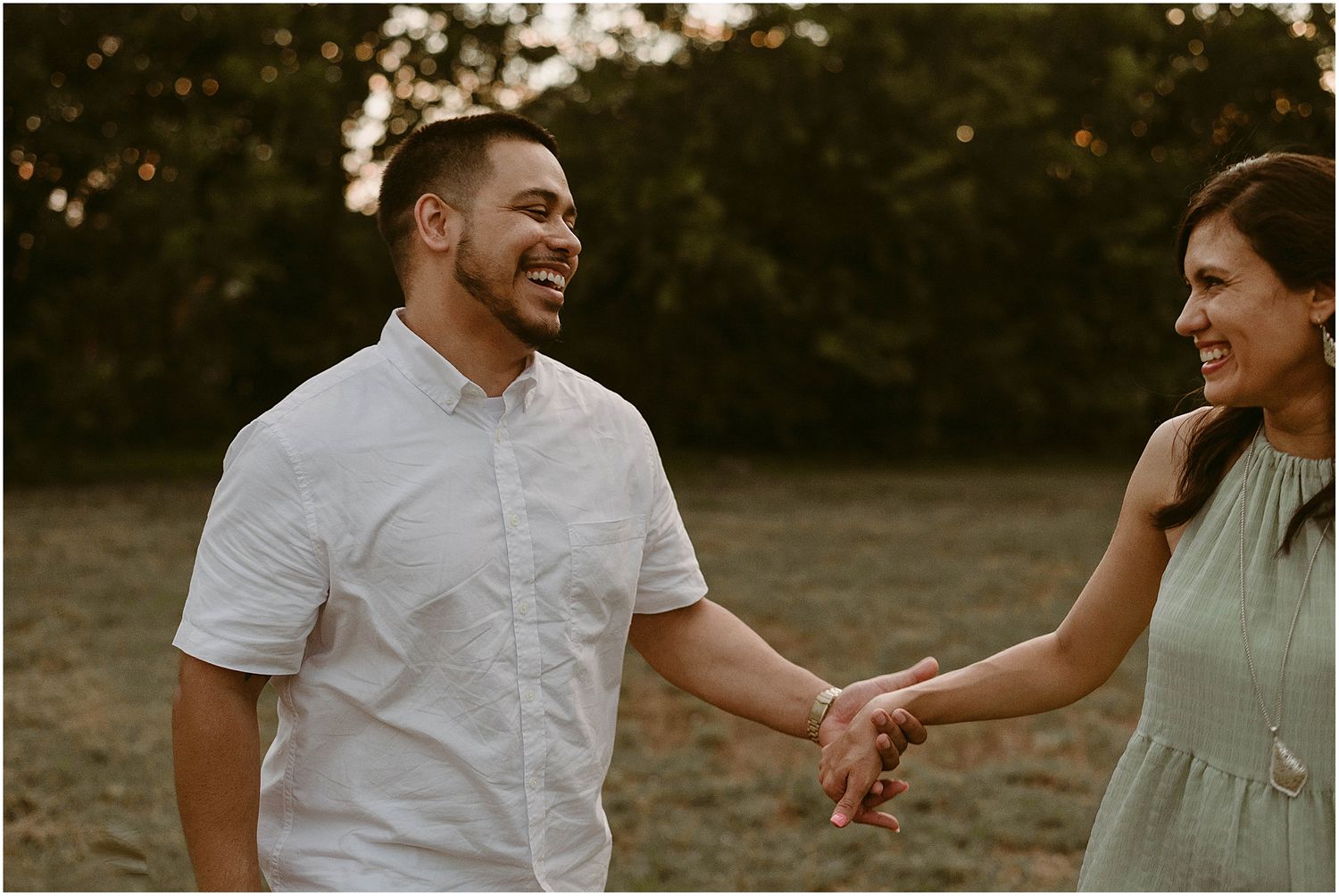 Carefree couple laughs together while holding hands during sunset photo session.