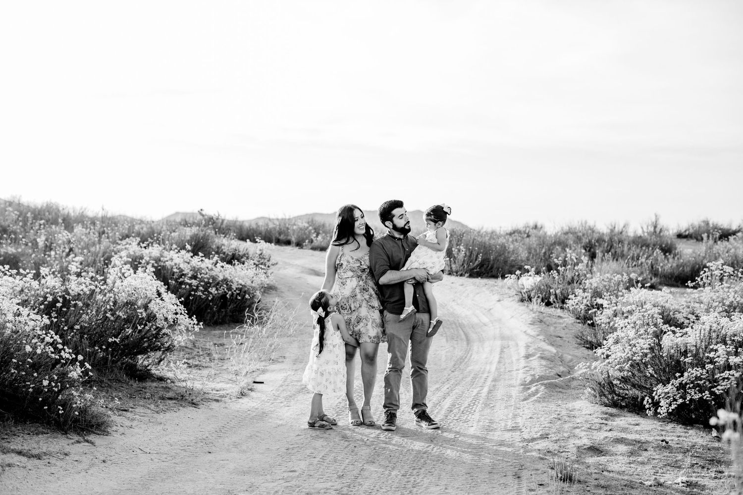 Family walking together on a desert path surrounded by blooming wildflowers in black and white.