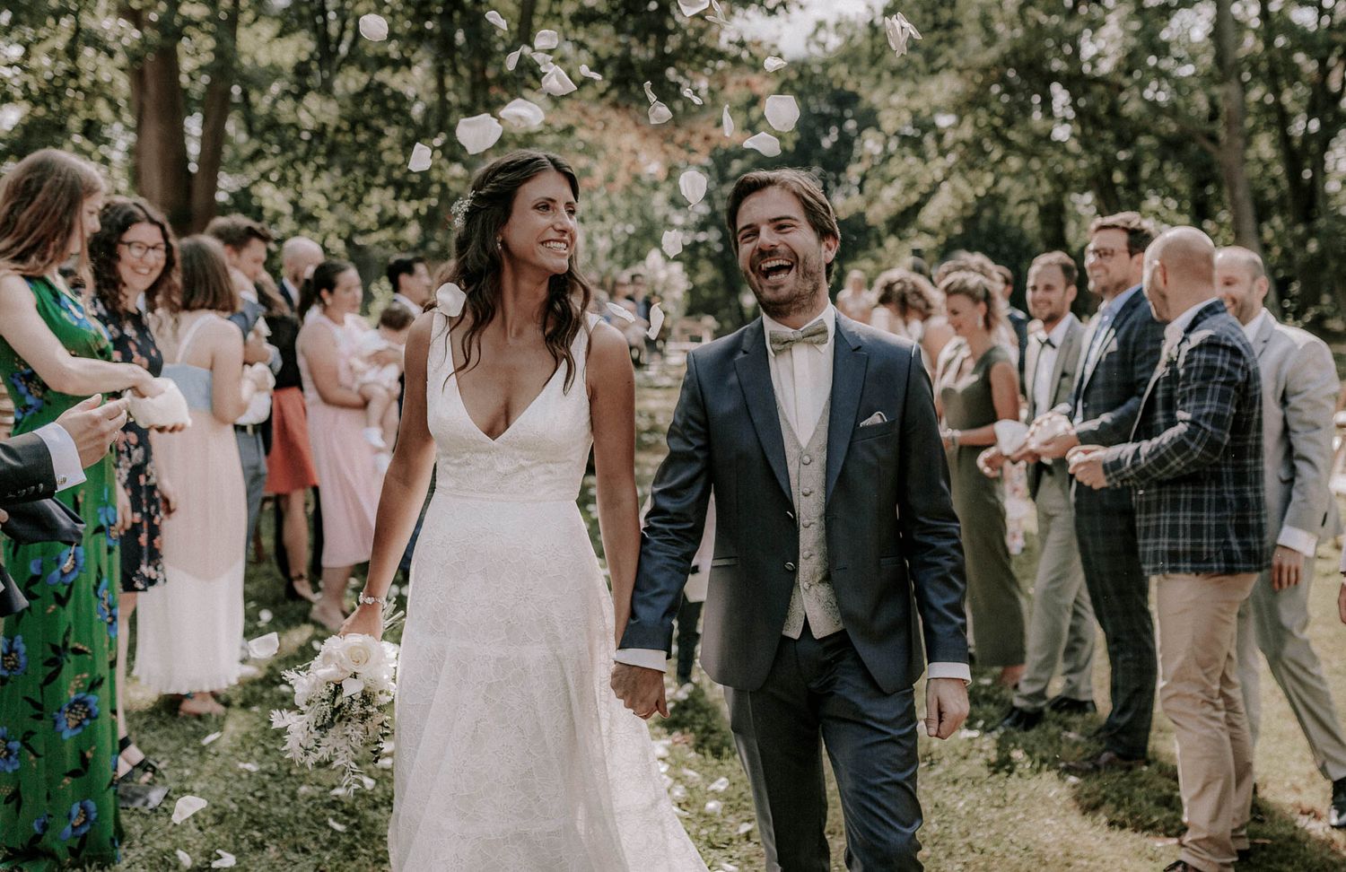 Joyful newlyweds walking through an outdoor garden celebration surrounded by wedding guests.