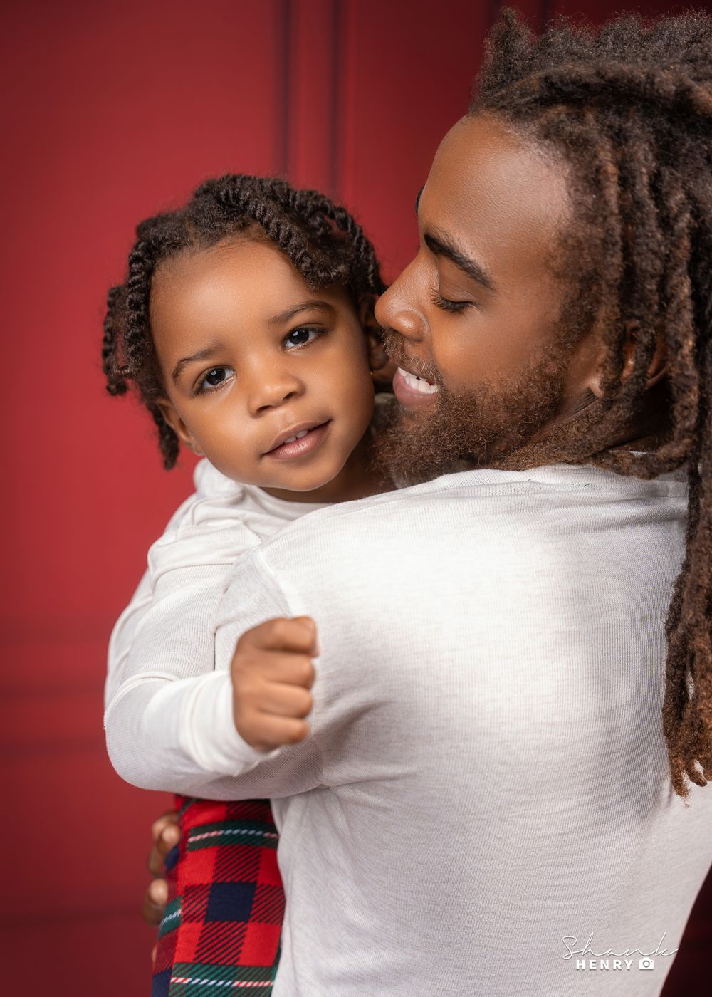 Intimate portrait of two people in white tops and plaid pants against red background.