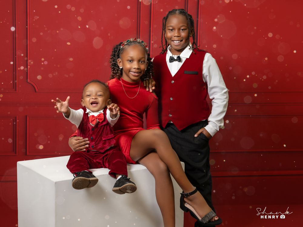 Holiday portrait with three people in red and black formal attire posing on white platform.