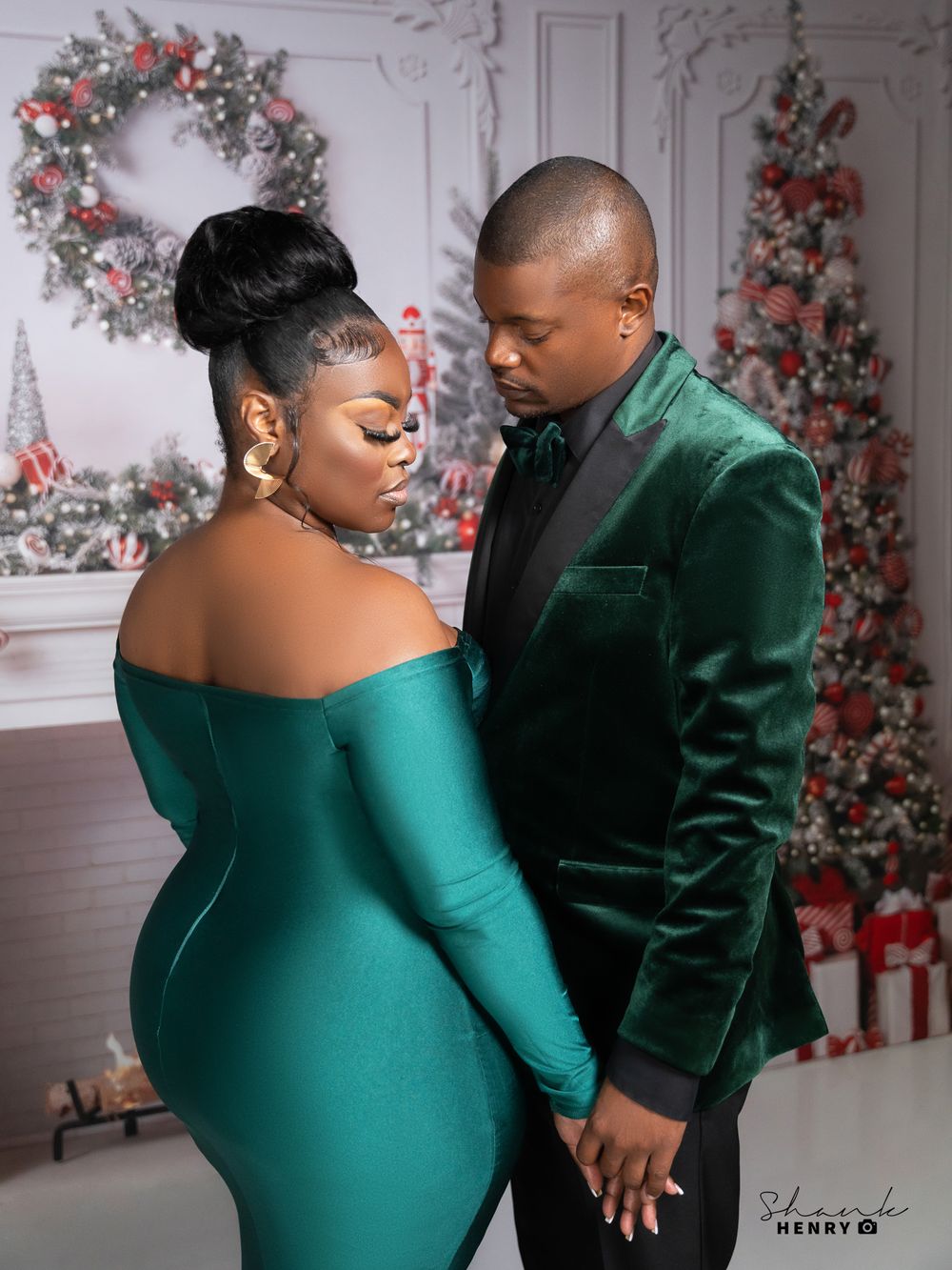 A couple in matching emerald green formal wear shares a romantic moment by Christmas decorations.