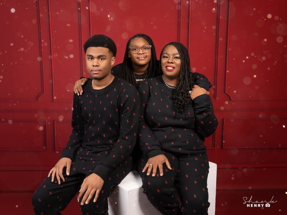Three people in black outfits pose for portrait against red backdrop with sparkle effect.