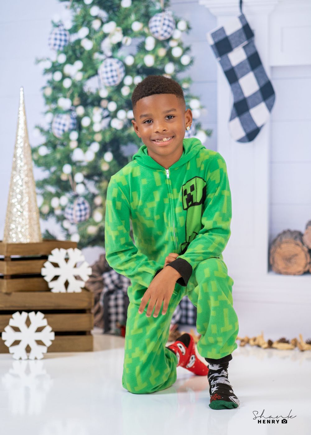Child in bright green tracksuit poses near Christmas tree with buffalo check stockings.