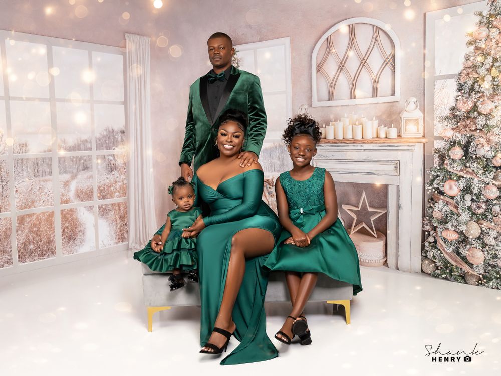 A family in elegant emerald green attire poses for a holiday portrait in front of a Christmas tree.
