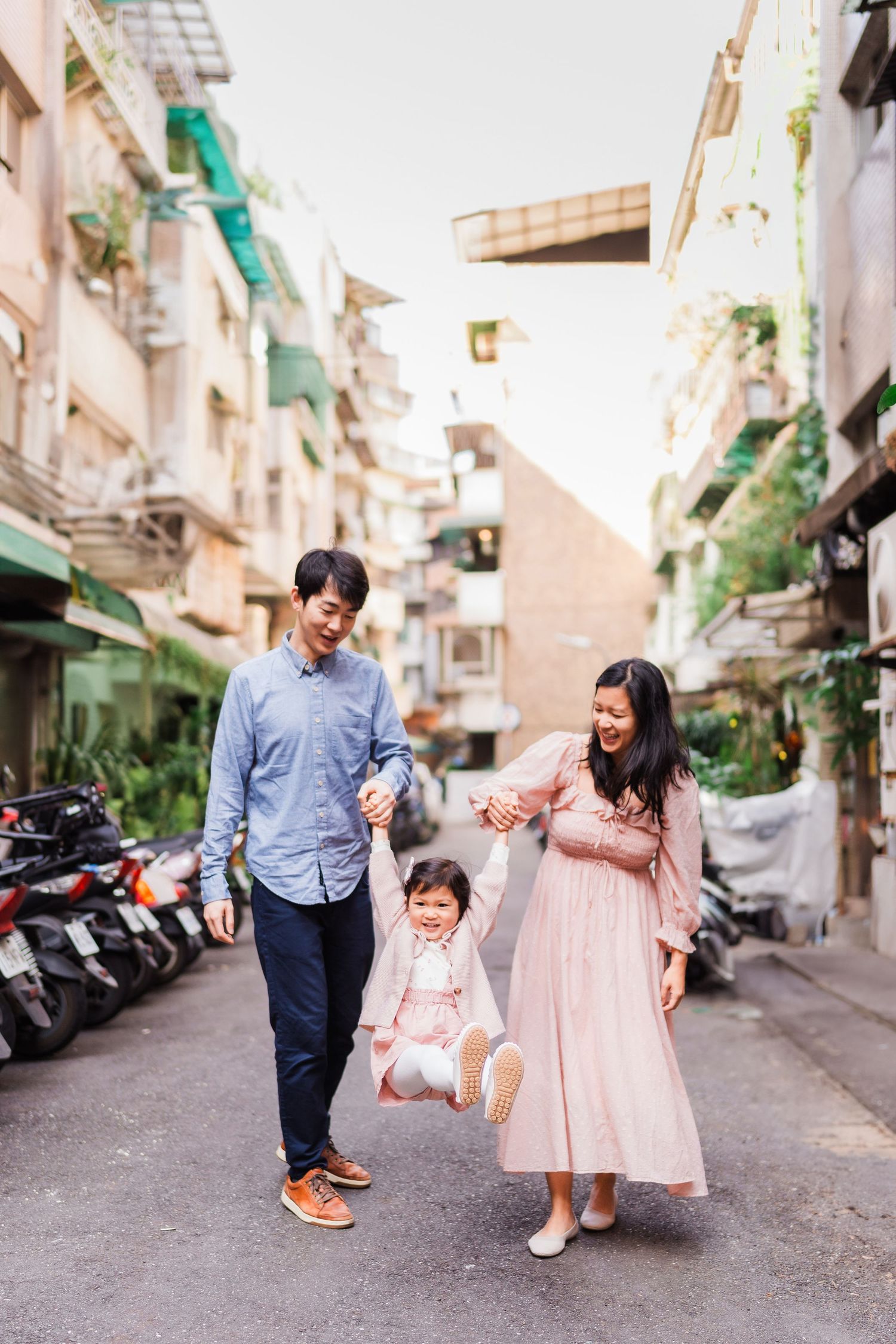 Family walking together in narrow alley lined with parked scooters.