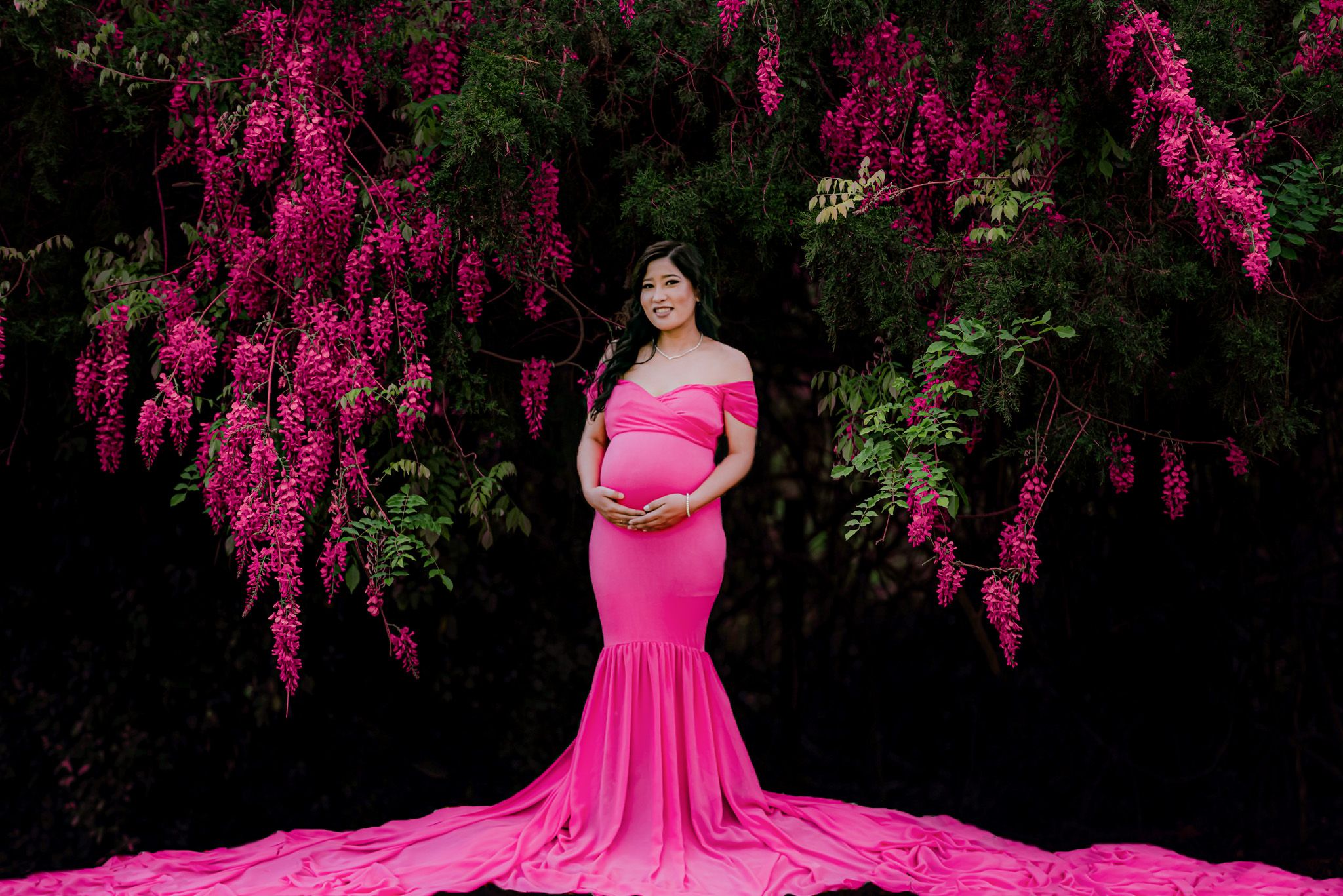 Maternity portrait with vibrant pink flowering trees creating a dramatic backdrop.