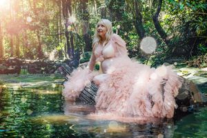 Flowing pink dress creates dreamy effect in garden maternity photo with water reflections.