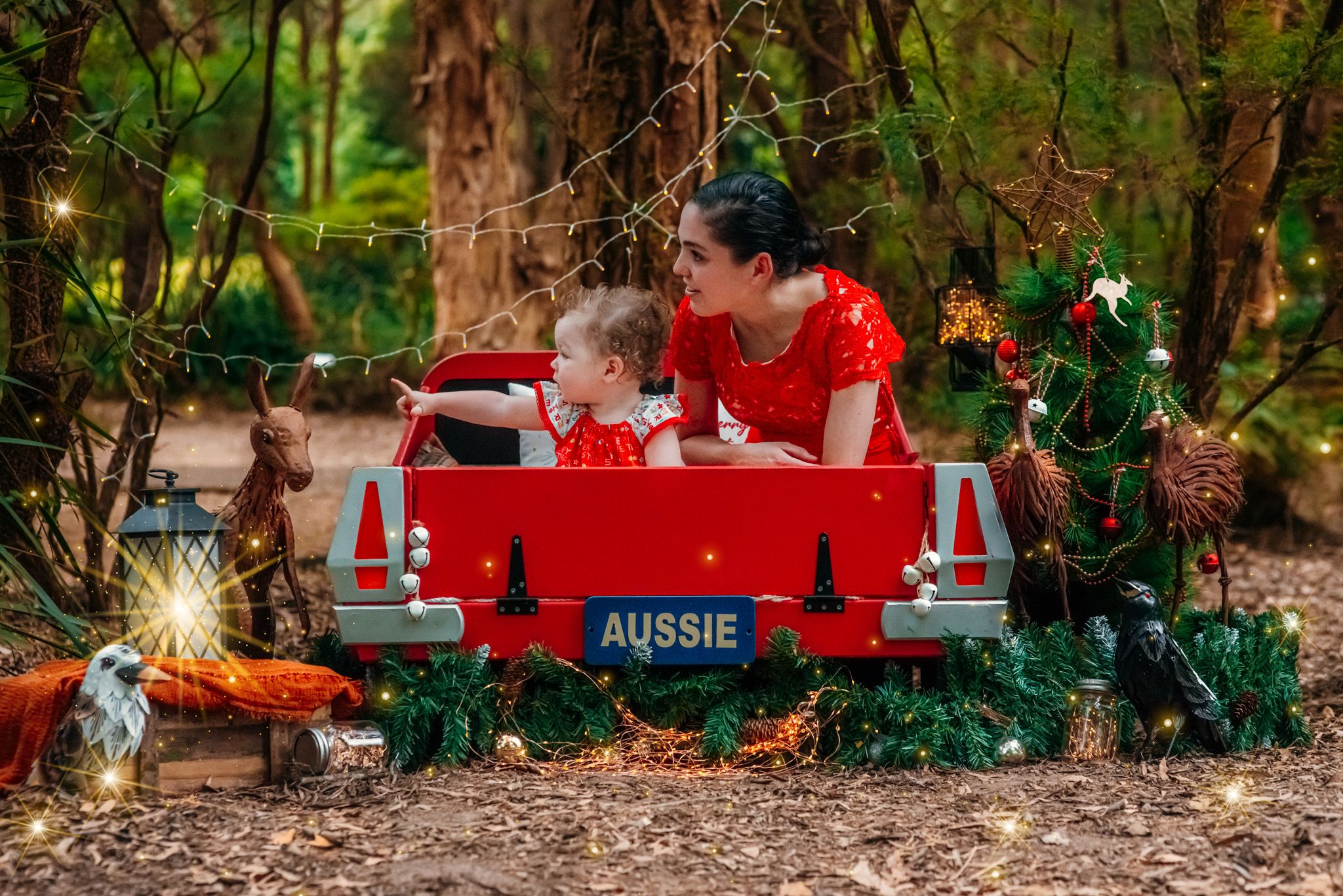 Festive red vintage truck decorated with Christmas trees and holiday decor in a woodland setting.
