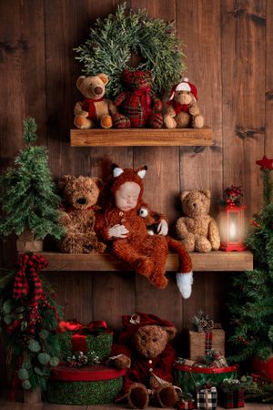 Cozy Christmas scene with teddy bears, evergreen branches and wooden shelves decorated for the holidays.