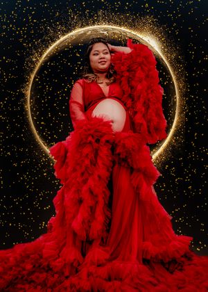 Dramatic maternity photoshoot featuring a flowing red tulle gown against a starry night sky background.