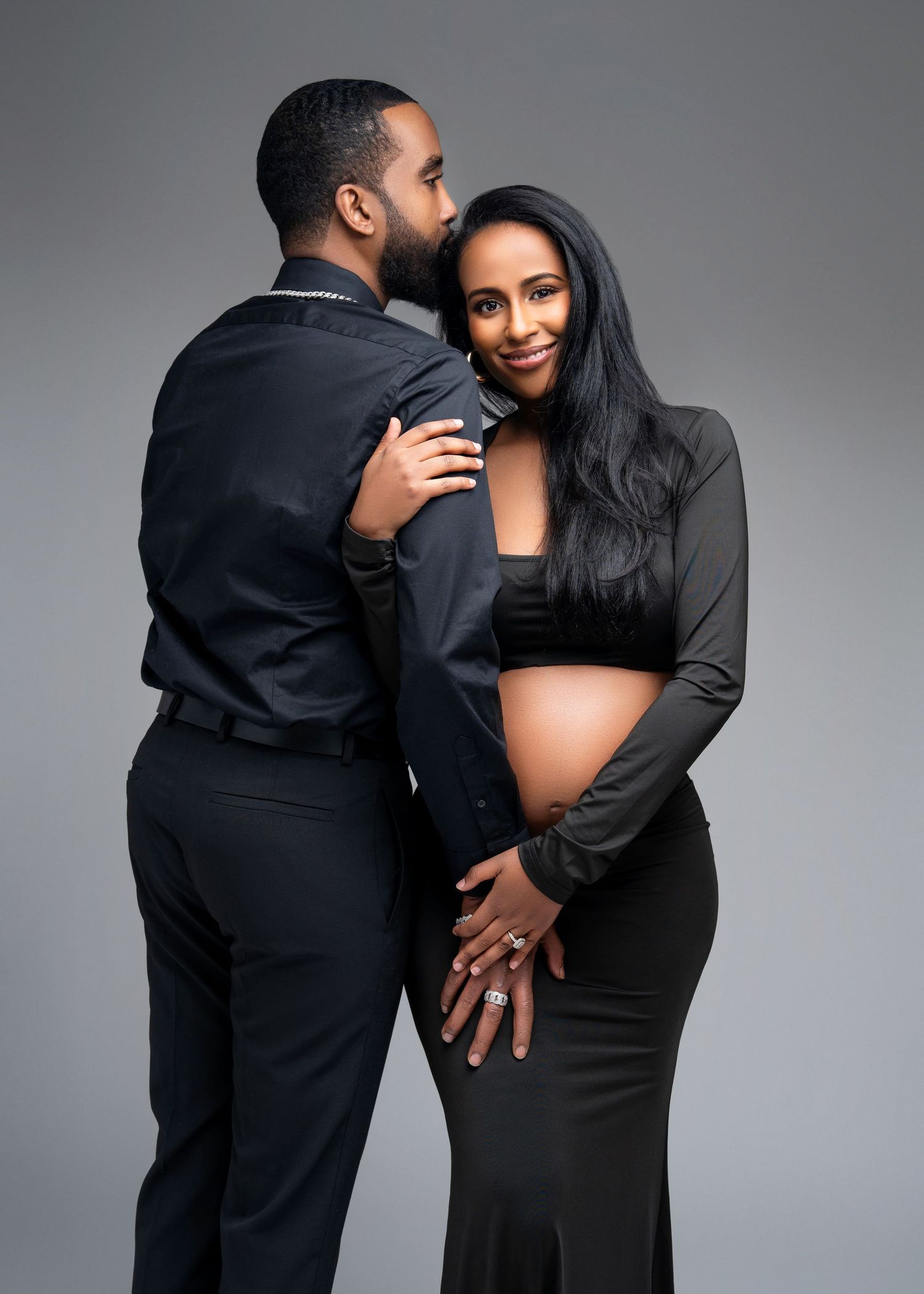 studio maternity photo shoot in Minneapolis Minnesota a couple stands, she rests her head on his shoulder and smiles